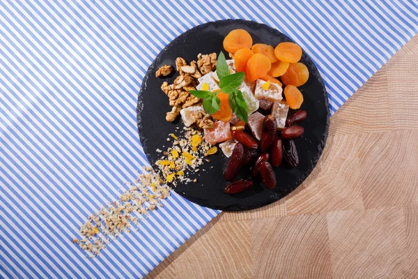 Siyah plaka yummies ve meyve dolu bir üstten görünüm renkli kumaş arka plan üzerinde. Kırmızı tarihi meyve, aromatik nane, Kuru Kayısı ve gevrek ceviz ile şekerli Türk lokumu. Kopya alanı.