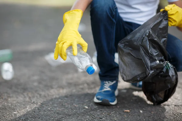 捡空瓶塑料垃圾袋上沥青 志愿者和纯度概念变成黄色带手套的手 环境保护 — 图库照片
