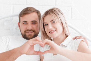 Aşk, insan ve mutluluk - çift yatakta, bir kalp şekil verme eller gülümseyen kavramı.