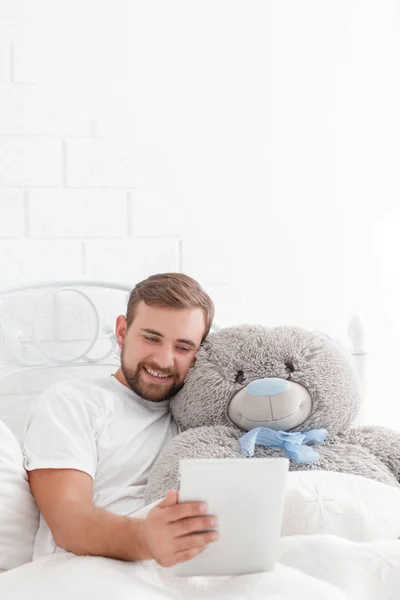 Портрет счастливого молодого человека с плюшевым мишкой, отдыхающего на кровати дома — стоковое фото