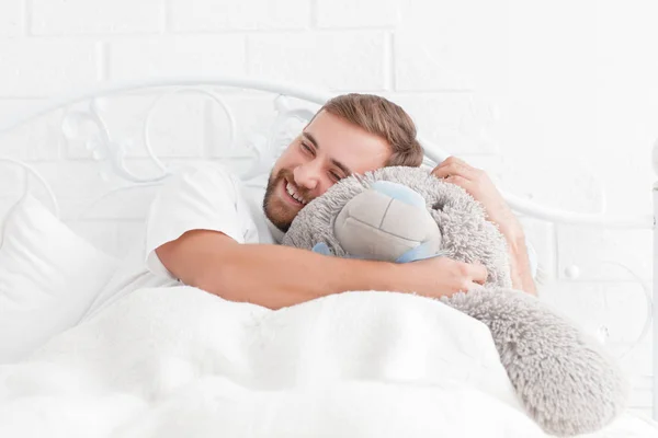 Молодой человек лежит в постели с плюшевым мишкой — стоковое фото