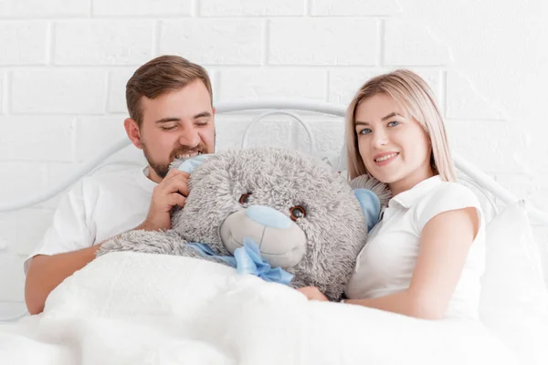 Casal jovem está com um ursinho de pelúcia na cama — Fotografia de Stock