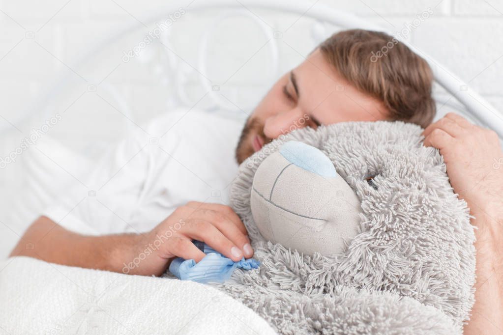 A young man sleeping with a teddy bear on the bed.