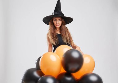 Sevimli cadı kız hafif bir arka plan üzerinde turuncu, siyah balonlarla. Cadılar Bayramı dekorasyon konsepti. Kopya alanı.