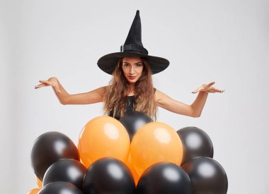 Sevimli cadı kız hafif bir arka plan üzerinde turuncu, siyah balonlarla. Cadılar Bayramı dekorasyon konsepti. Kopya alanı.