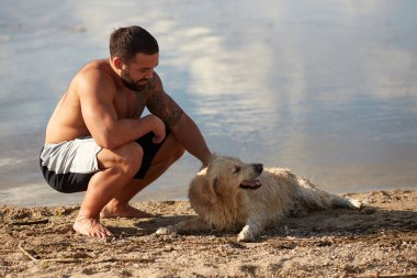 Bir adam köpeğini bir nehir arka planı okşayarak