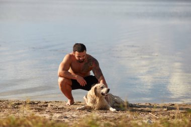 Bir adam köpeğini bir nehir arka planı okşayarak