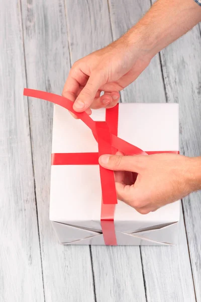 Las manos que unen la cinta en una caja de regalo blanca, vista superior — Foto de Stock