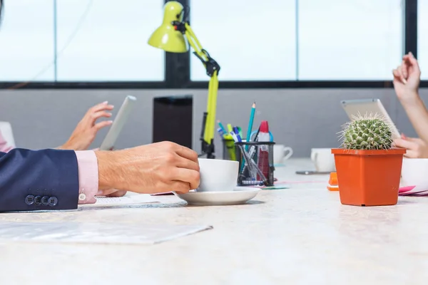 De werknemers hand houdt een kopje koffie aan tafel — Stockfoto