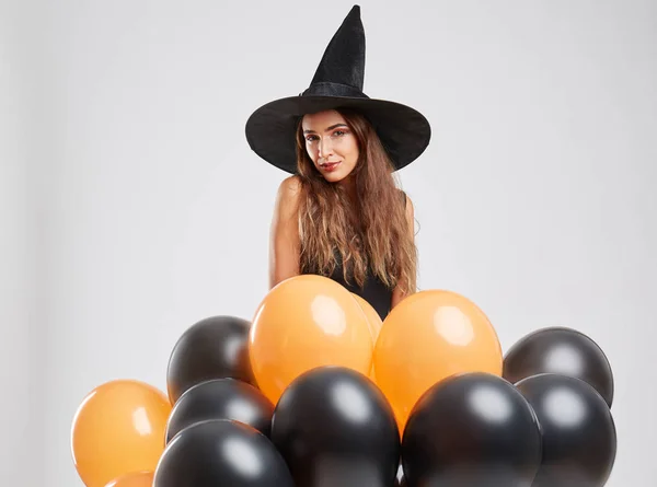 Schattig heks meisje met oranje, zwarte ballonnen op een lichte achtergrond. Halloween decoratie concept. Kopiëren van ruimte. — Stockfoto