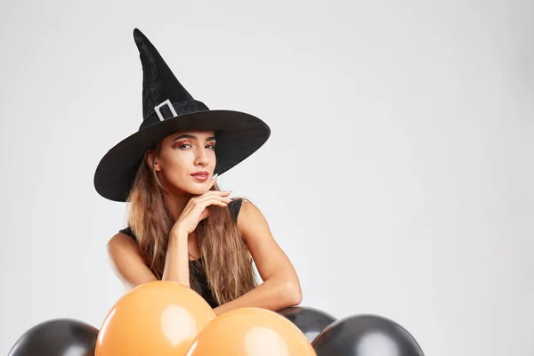 Cute witch girl with orange, black balloons on a light background. Halloween decoration concept. Copy space. — Stock Photo, Image