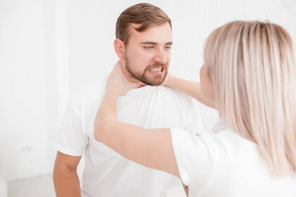 Uma menina está estrangulando um homem em um fundo branco — Fotografia de Stock