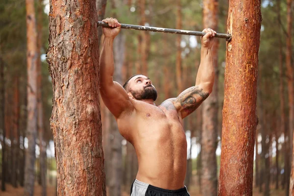 Een jonge sterke atleet trekt in het bos. — Stockfoto