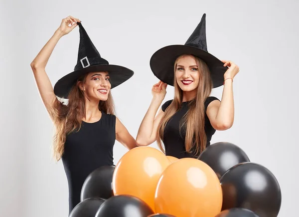 Halloween witch girls celebrating with balloons on a light background. Halloween party concept.