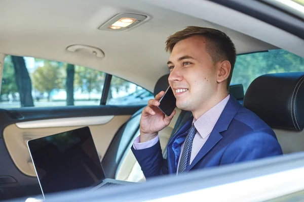 Telefonda konuşurken bir dizüstü bilgisayar ile arabasında işadamı