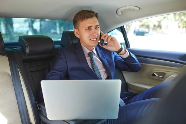 Biznesmen w swoim samochodzie z laptopa rozmawiać przez telefon — Zdjęcie stockowe
