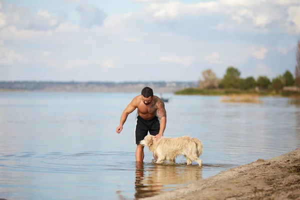 Een man rommelt met een hond in het water — Stockfoto