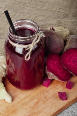 Bir mason kavanoza beetroots sağlıklı suyu dolu bir bileşimi üstten görünüm bir kesme tahtası üzerinde. Bir kaç dilim pancar ve zencefil bir kumaş ve ahşap arka plan. Organik pişirme maddeler.