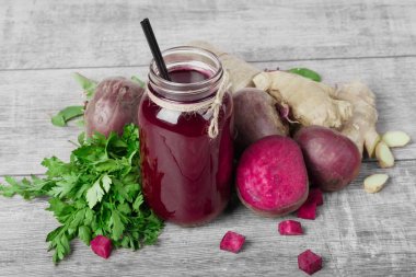 Bir büyük mason kavanoza pancar suyu ile siyah saman dolu güzel bir kompozisyon üstten görünüm gri bir ahşap zemin üzerinde. Bütün ve kesme kırmızı pancar, taze yeşil maydanoz ve zencefil masada.