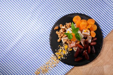 Siyah plaka yummies ve meyve dolu bir üstten görünüm renkli kumaş arka plan üzerinde. Kırmızı tarihi meyve, aromatik nane, Kuru Kayısı ve gevrek ceviz ile şekerli Türk lokumu. Kopya alanı.