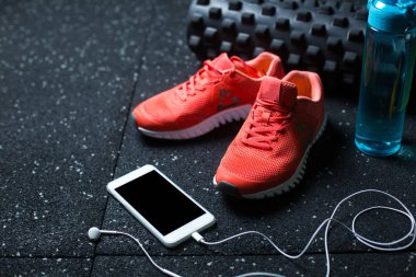 Bir mavi plastik şişe su, kulaklık ve pembe parlak spor ayakkabılar bulanık koyu arka plan üzerinde beyaz bir cep telefonuyla için.