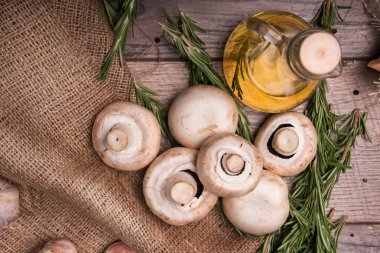 Ahşap arka plan üzerinde bir ormandan gelen taze beyaz mantar bir yığın bir manzara yukarıdan. Ayçiçeği yağı, yeşil biberiye ve masanın üzerine eski bir kahverengi çanta üzerinde baharatlı sarımsak dolu vazo.