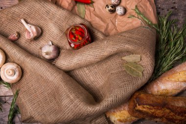 Üstten Görünüm taze mantar, yeşil defne yaprağı ve doğal biberiye buruşturulmuş bir kağıt ve bir ahşap arka plan. Kahverengi kumaş üzerine bir kavanoz, kırmızı biber, güzel kokulu sarımsak, pişmiş ekmek ve Bıldırcın yumurta.