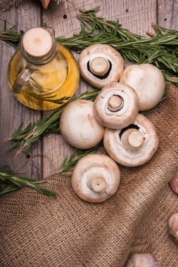 Şeffaf şişe dolu güzel kokulu zeytin yağı ve dalları yeşil biberiye üstten görünüm ahşap arka plan üzerinde. Sonbahar ormandaki bir çanta ve masanın üzerinde bir kaç taze ve organik mantar.