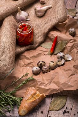 Üstten Görünüm bir kompozisyon, şeffaf bir kavanozu sıcak kırmızı biber, sarımsak ve bıldırcın dolu bir kahverengi kumaş ve ahşap arka plan üzerinde yumurta. Bir yığın beyaz mantar ve bir dilim ekmek bir masa üzerine.