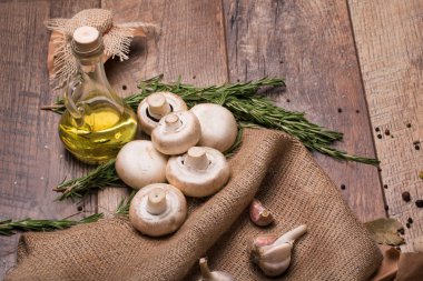 Kahverengi ahşap arka plan üzerinde büyük doğal beyaz mantar ve sarımsak bir resim bir görüntü yukarıdan. Şeffaf bir kapasite sarı ayçiçeği yağı ve rustik kumaş üzerinde taze biberiye dolu.