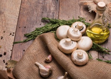 Kahverengi ahşap arka plan üzerinde büyük doğal beyaz mantar ve sarımsak bir resim bir görüntü yukarıdan. Şeffaf bir kapasite sarı ayçiçeği yağı ve rustik kumaş üzerinde taze biberiye dolu.