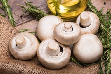 Büyük doğal beyaz mantar kahverengi ahşap arka plan üzerinde yakın çekim resmin. Şeffaf bir kapasite sarı ayçiçeği yağı ve dal taze biberiye rustik kumaş üzerinde dolu.