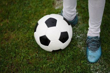 Parlak yeşil çim zemin üzerine yukarıdan görünüm tek futbol topu ve adamın ayak spor ayakkabı. Yeşil bir alana bir yuvarlak siyah beyaz futbol topu. Açık havada faaliyetleri. Kopya alanı.