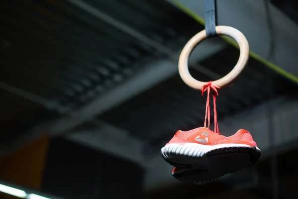 Crimson bright sneakers hanging on steady wooden ring. Sports concept.