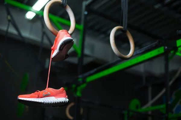Wooden steady ring with sneakers hanging on it on pink shoelaces, equipment for a gym, sports routine on a dark blurred background.
