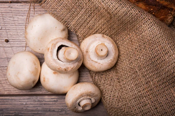 A view from above of fresh and raw white mushrooms on a rustic wooden counter. Tasteful, raw champignons for cooking on a brown bag and on a wooden background. Healthful concept.