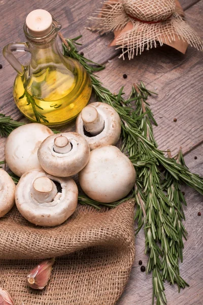Şeffaf şişe dolu güzel kokulu zeytinyağı, sarımsak ve dallar yeşil biberiye üstten görünüm ahşap arka plan üzerinde. Ormandaki bir çanta ve masanın üzerinde bir kaç taze ve organik mantar.