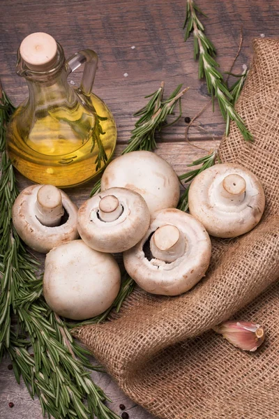 Şeffaf şişe dolu güzel kokulu zeytinyağı, sarımsak ve dallar yeşil biberiye üstten görünüm ahşap arka plan üzerinde. Ormandaki bir çanta ve masanın üzerinde bir kaç taze ve organik mantar.