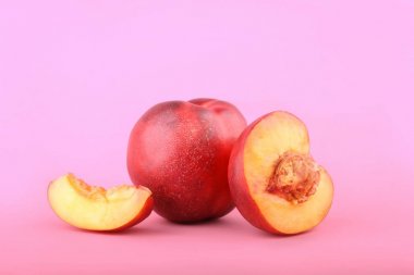 Bir bütün ve kesilmiş taze kırmızı nektarin close-up. Olgun, parlak, parlak pembe bir arka plan üzerinde meyve yenileniyor. Portakal şeftali sulu bir dilim. Yaz meyve. Kopya alanı.