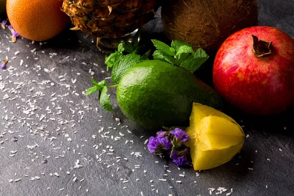 Tropikal meyve üzerinde arka planı gri taş ayarla close-up. Parlak avokado, sarı carambola, olgun garnet, egzotik Hindistan cevizi ve tropikal ananas. 