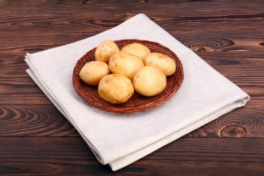 Gerdanlı bir plaka, genç yeni ve ham patates unpeeled patates lezzetli kursları, büyüme, sağlık ve iyi durumda bir koyu kahverengi zemin üzerinde gerekli maddeler içeren sebze için.