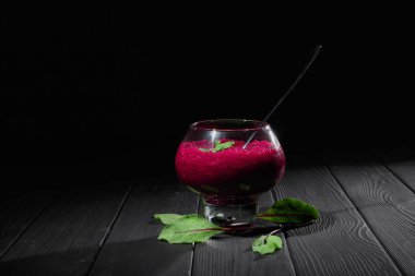 Bir bordo renkli pancar güler yüzlü büyük şeffaf tatlı kadeh kokteyl. Bir cam sağlıklı sebze siyah tablo arka plan üzerinde kokteyl ile dolu. Pancar içecek yeşil yaprakları ile. Kopya alanı.