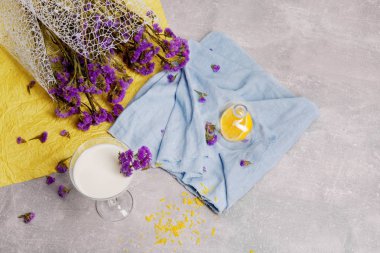 Yukarıdan bir görünümü temel bir margarita cam gri tablo arka plan üzerinde süt kokteyl ve renkli kumaş dolu. Bir bardak dekoratif çiçeklerle milkshake. Mor bir buket ile serinletici yüzlü.
