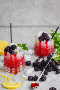 Süslü gözlük tam soğuk, buzlu içecekler baharatlı nane, limon parçaları, sulu böğürtlen ve gri taş zemin üzerine siyah çöp. Reçel kaşıkla iki serinletici kokteyller. Kopya alanı.