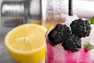 Yakın çekim resmini bir buzlu içecek Ekşi limon ve böğürtlen üzerinde metal arka plan bulanık. Olgun, taze böğürtlen ve bir kesim sarı limon için soğuk bir yüzlü. Parti konsept.