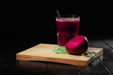 Güzel kırmızı pancar suyu bir bardak siyah bir arka plan. Büyük bir pay yarım pancar ve ahşap kesme masa üzerinde taze salata. Pahalı bitkisel kokteyller. Tazelik, sağlık, doğa kavramı. Kopya alanı.