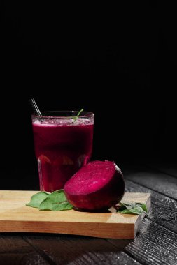 Güzel kırmızı pancar suyu bir bardak siyah bir arka plan. Büyük bir pay yarım pancar ve ahşap kesme masa üzerinde taze salata. Pahalı bitkisel kokteyller. Tazelik, sağlık, doğa kavramı. Kopya alanı.