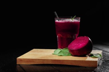Güzel kırmızı pancar suyu bir bardak siyah bir arka plan. Büyük bir pay yarım pancar ve ahşap kesme masa üzerinde taze salata. Pahalı bitkisel kokteyller. Tazelik, sağlık, doğa kavramı. Kopya alanı.