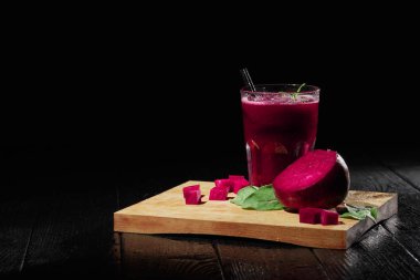 Saydam bir cam ile büyük, kalın bir kırmızı yüzlü yarım pancar kesmek dolu ve bir siyah tablo arka plan üzerinde doğal, yeşil salata yaprakları. Taze pancar mükemmel küplerinde kesti. Kopya alanı.