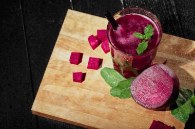 Dan yukarıda kırmızı ile dekoratif baharat ve payet, sulu, kokteyl ile bir bardak güzel bir dizi yarım kırmızı pancar, pancar küpleri ve salata yaprakları siyah bir arka plan kesme masasında dilimlenmiş görüntüleyin.